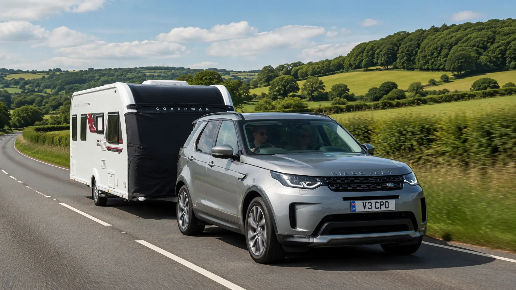 Alt Text: Silver Land Rover Discovery towing a white Coachman Sussex Singleton caravan on an English country road