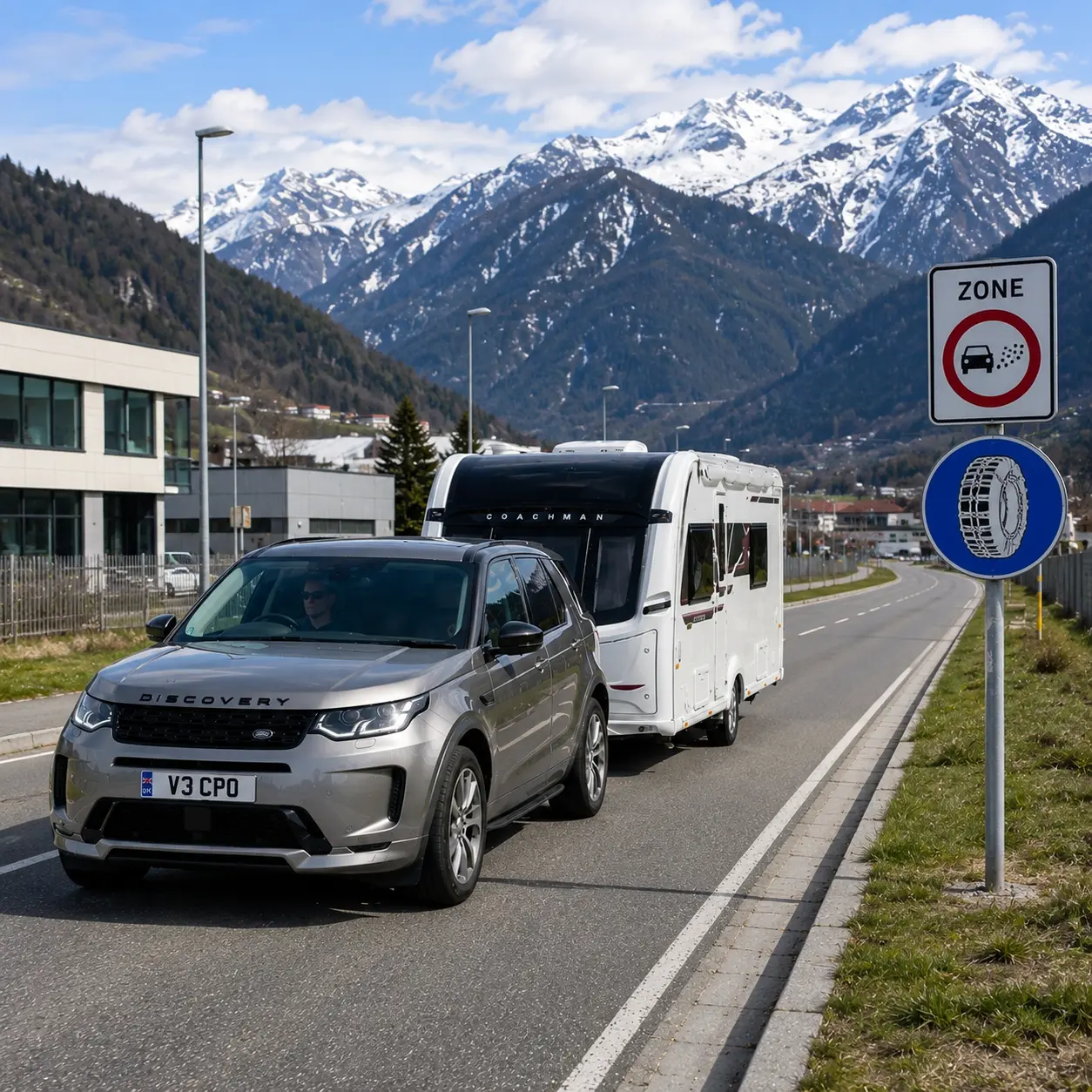 Silver Land Rover Discovery towing a Coachman caravan past European low-emission and snow-chain road signs